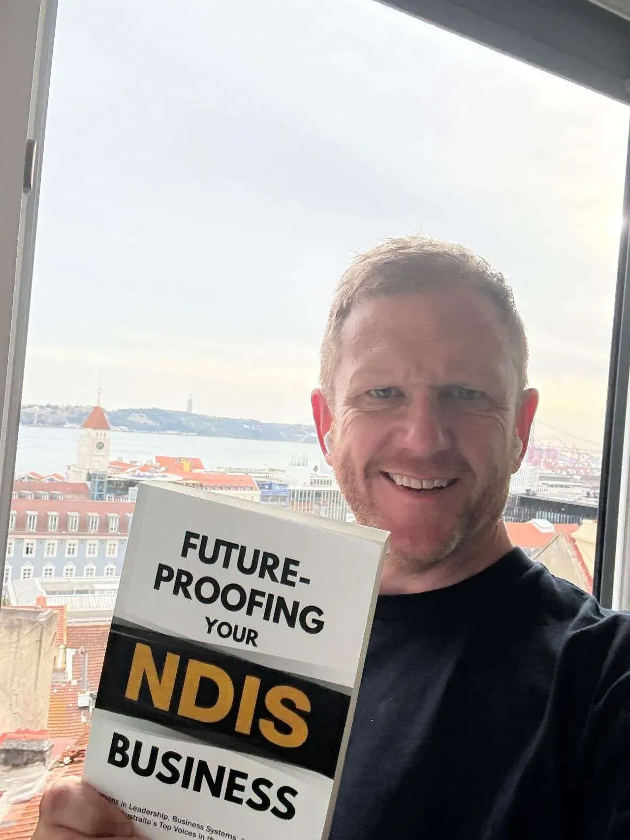 Man holding a “Future-proofing our NDIS business” sign, smiling by a bright window.