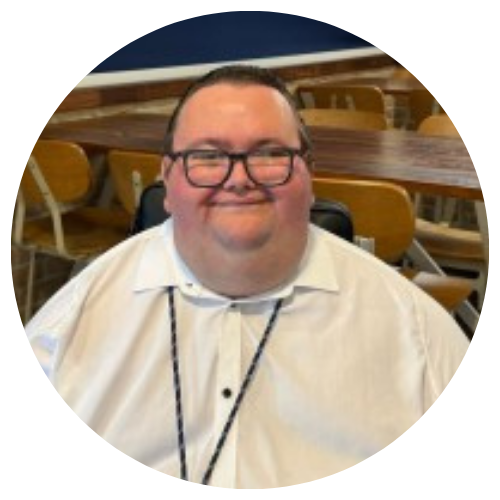 Smiling person in glasses and a white shirt seated in a wooden church or hall interior