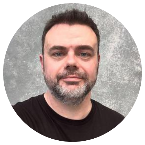 Head-and-shoulders portrait of a man with short dark hair and a salt-and-pepper beard against a gray background