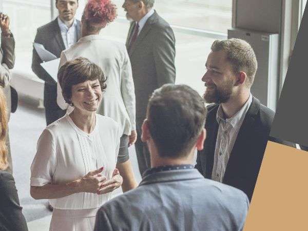 Small group networking in a bright office, with people chatting and smiling near a window.
