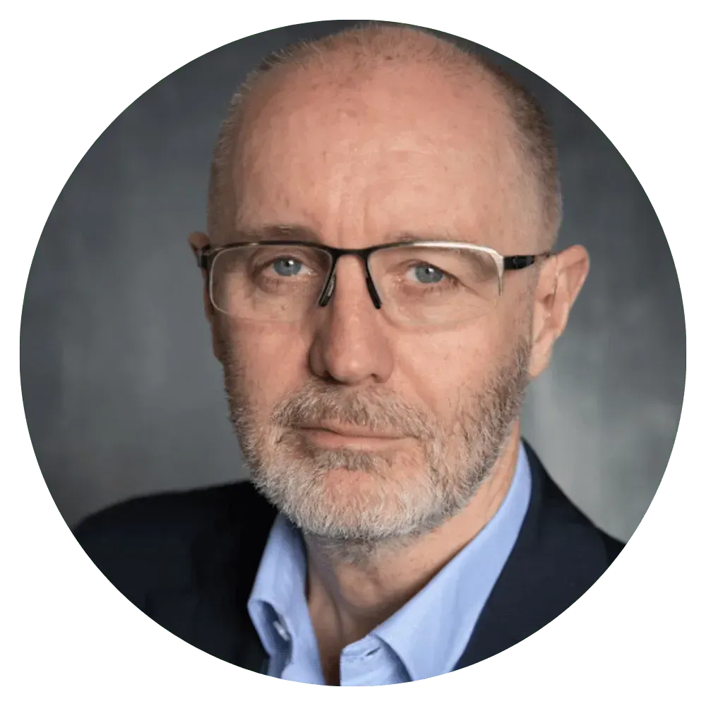 Studio headshot of a bald man with glasses and a gray beard, wearing a blue shirt and dark blazer.