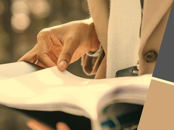 Hands flipping through papers at a desk with a blurred beige jacket in warm light