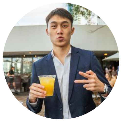 Man in a navy blazer holding a yellow drink and making a peace sign at an outdoor cafe