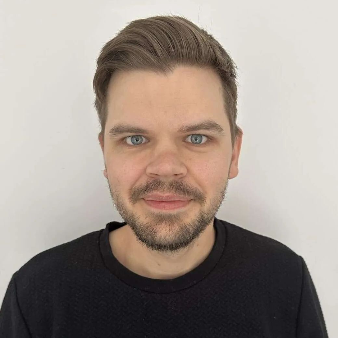 Portrait of a smiling man with short brown hair and beard against a plain white background