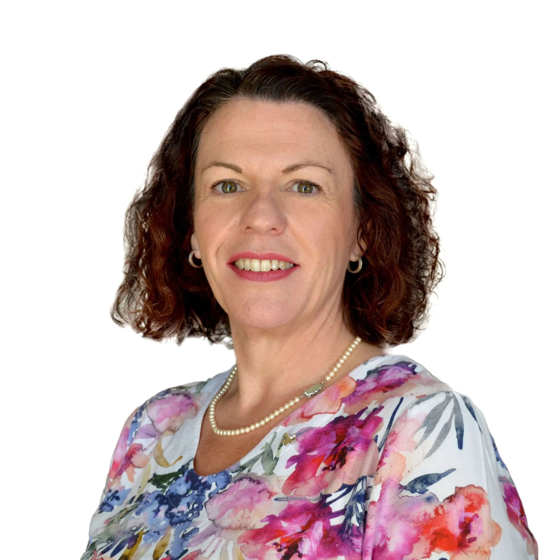 Studio portrait of a smiling woman with curly dark hair wearing a floral blouse and pearl necklace