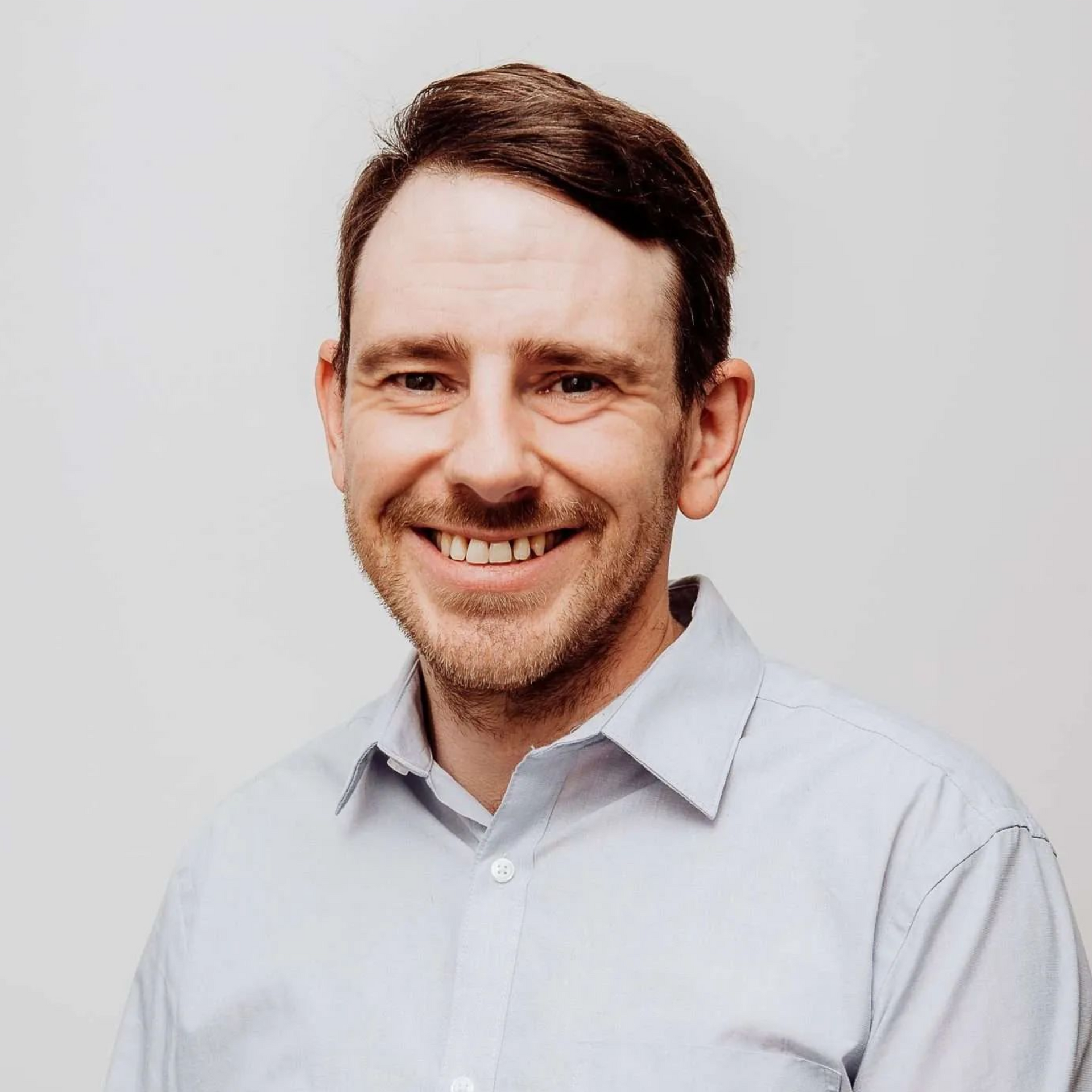 Smiling man in a light blue shirt against a plain gray background
