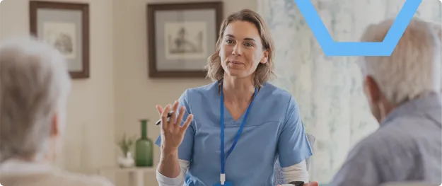 Healthcare worker in blue scrubs speaking to two seated patients in a clinic room