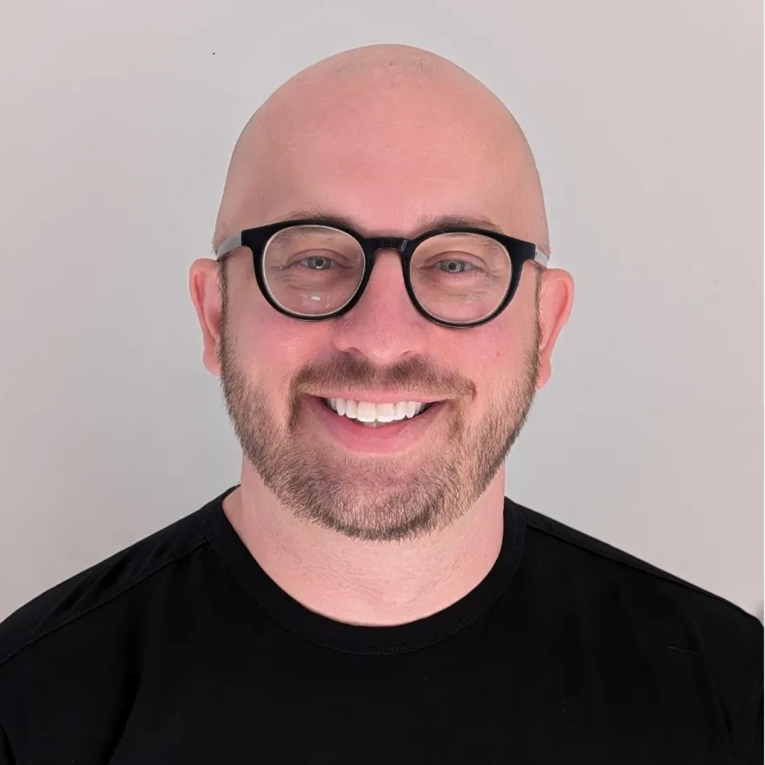 Smiling bald man with glasses in a black shirt against a light background