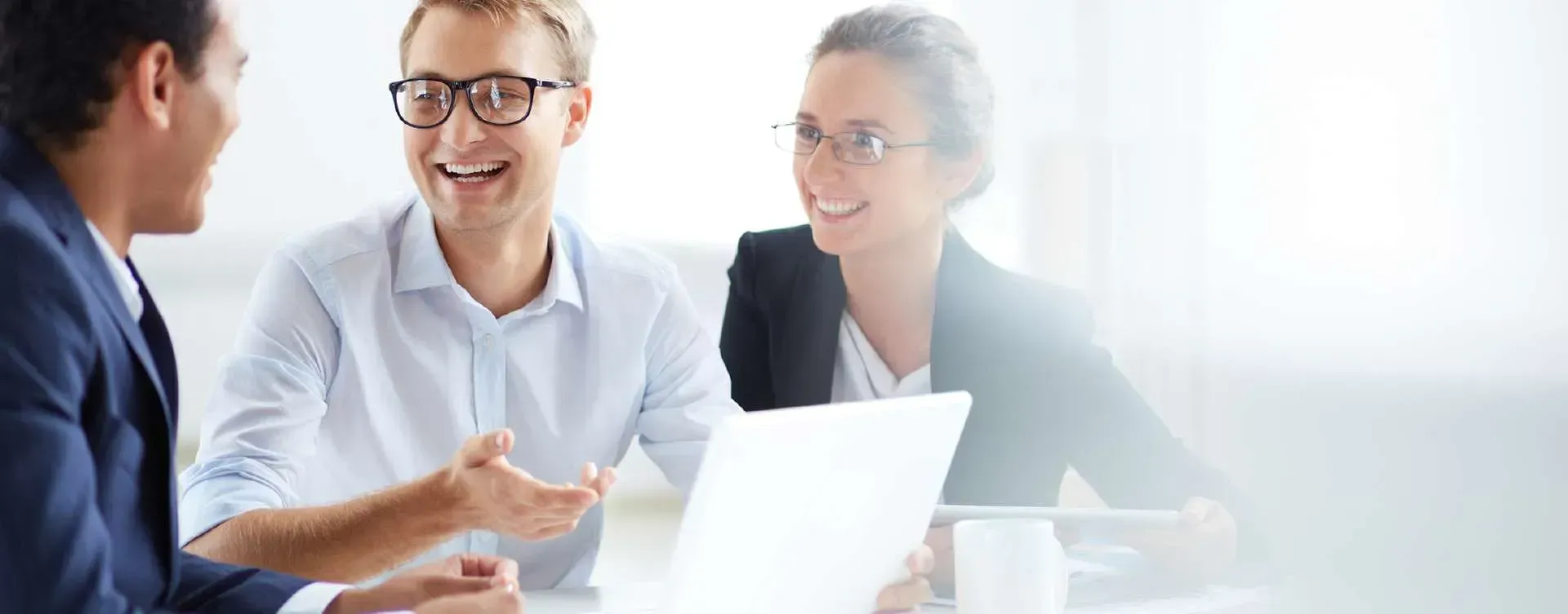 Three coworkers in a bright meeting room discussing ideas around a laptop