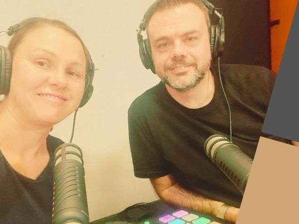 Two people wearing headphones speak into microphones in a podcast studio.
