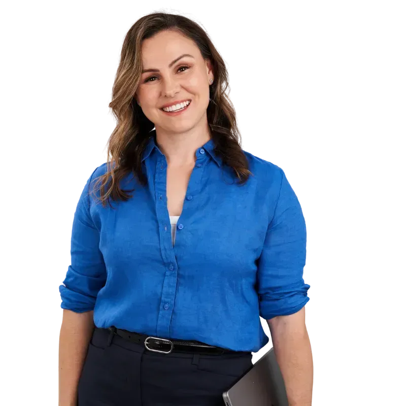Smiling woman in a blue blouse and dark pants, standing against a white background.