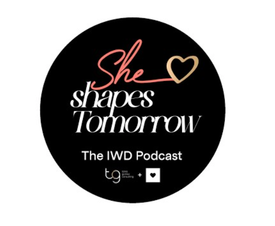 Black circular logo reading “She shapes Tomorrow” and “The IWD Podcast” in pink and white with a heart icon