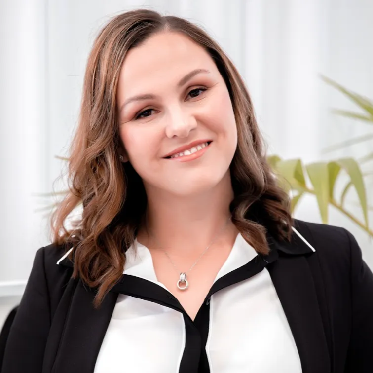 Smiling woman in a black blazer and white blouse, posed in a bright office setting