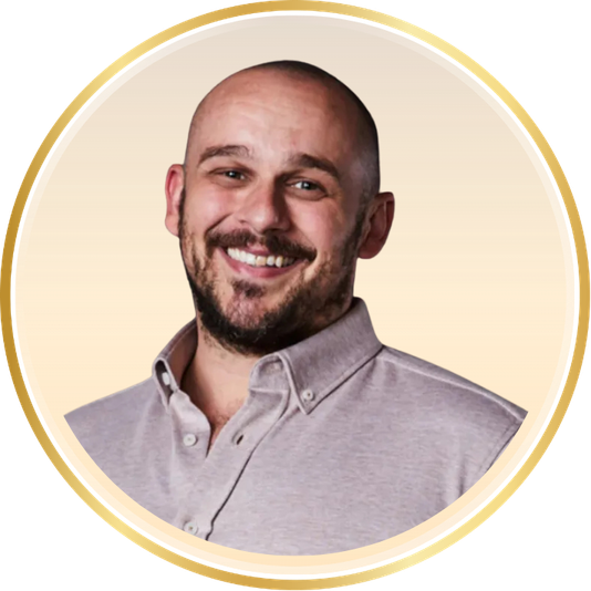 Smiling bald man in a light button-up shirt, framed in a circular gold border on a pale background