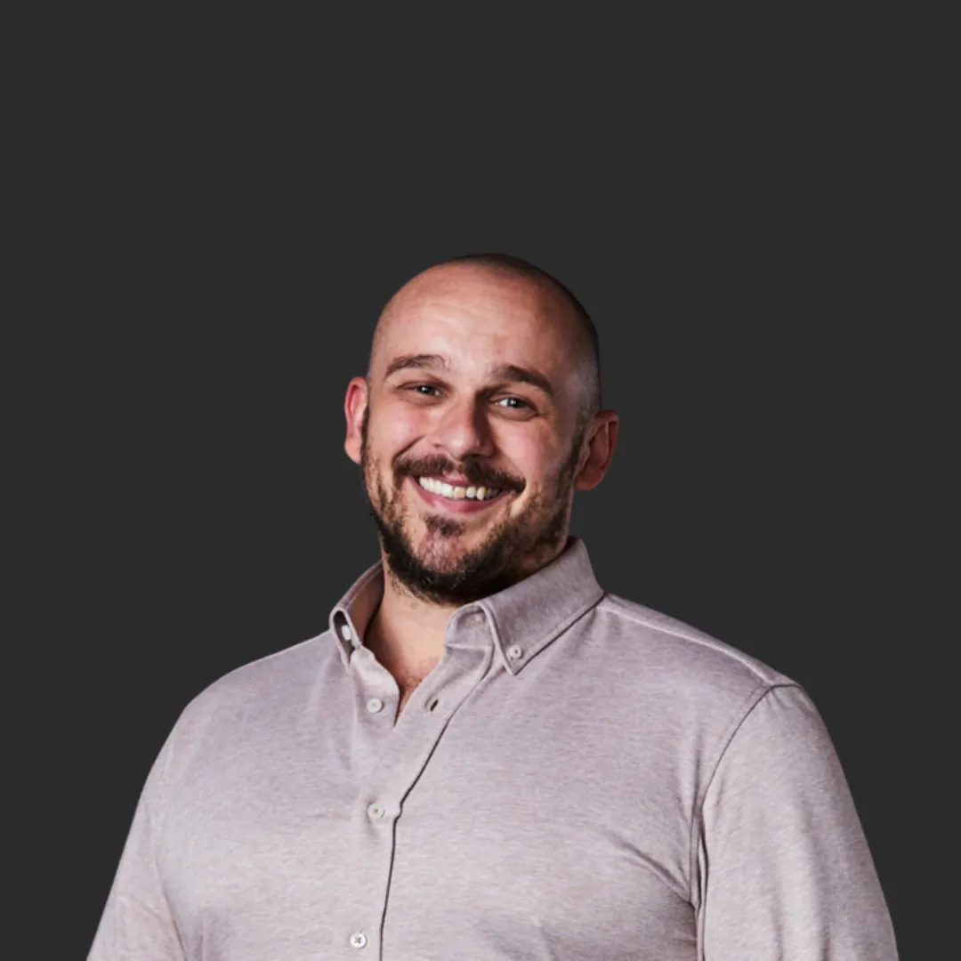 Smiling bald man in a light gray button-up shirt against a dark background