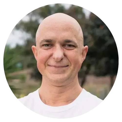 Portrait of a smiling bald man in a white shirt outdoors, with a blurred green background