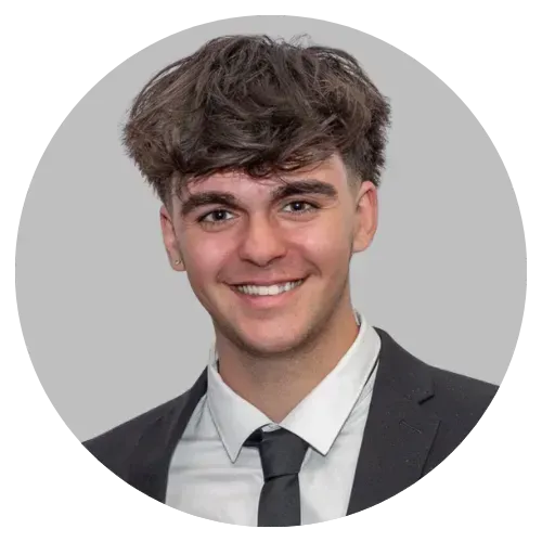 Smiling person in a dark suit and tie against a light gray background