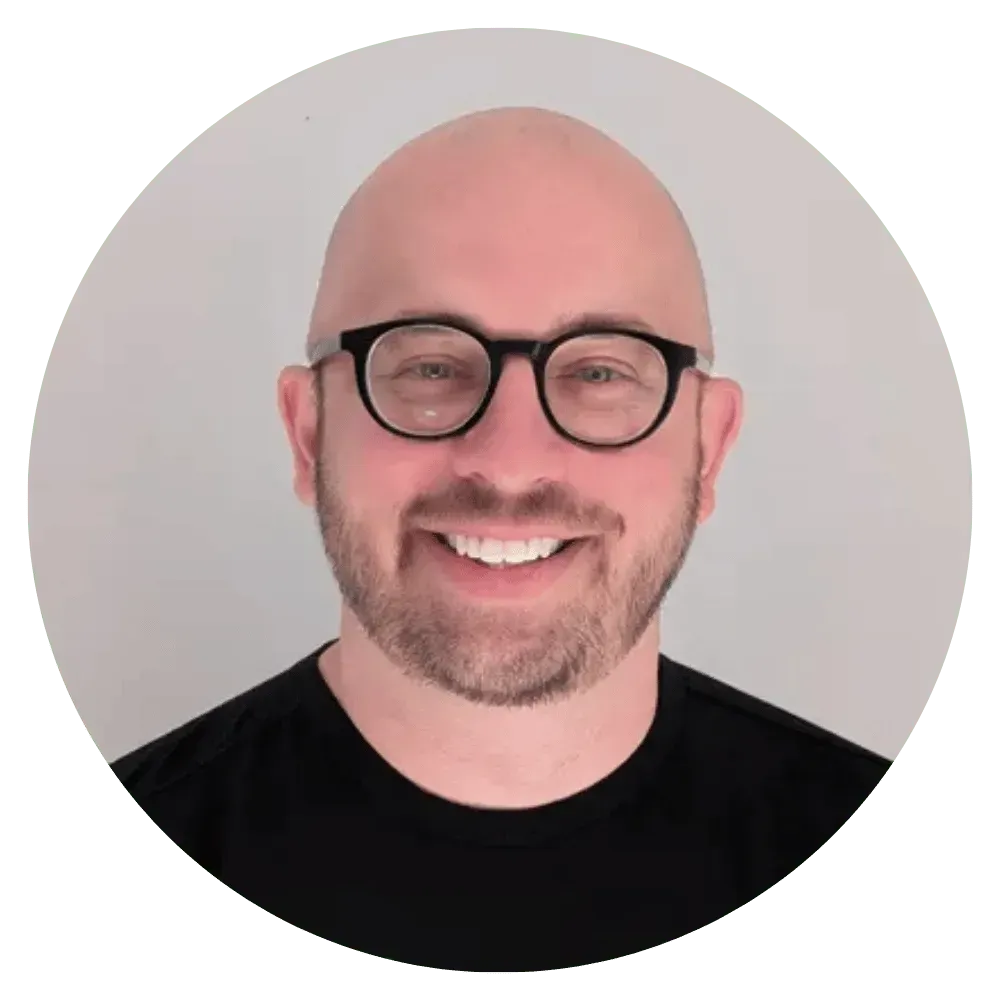Smiling bald man with glasses in a black shirt against a light gray background