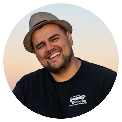 Smiling man in a gray hat and black shirt against a soft sunset sky background