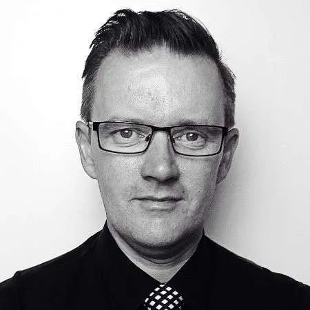 Black-and-white portrait of a man wearing glasses, a dark shirt, and patterned tie