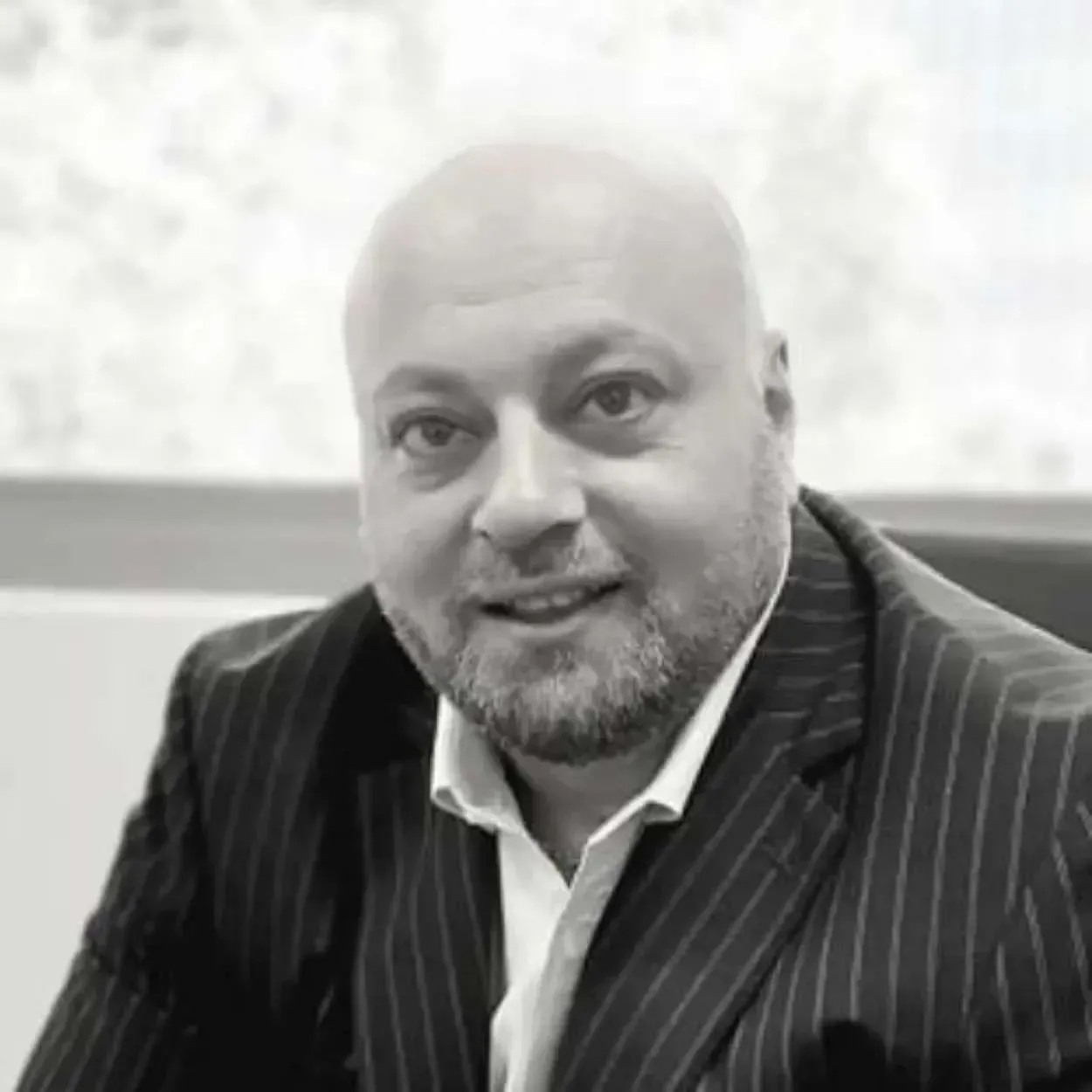 Portrait of a smiling bald man in a dark pinstripe suit and white shirt