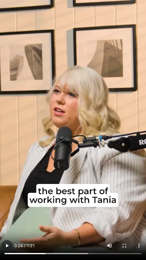Blonde woman speaking into a microphone in a podcast studio, with framed art on the wall and caption text overlay.