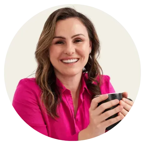 Smiling woman in a bright pink blouse holding a black mug against a light background