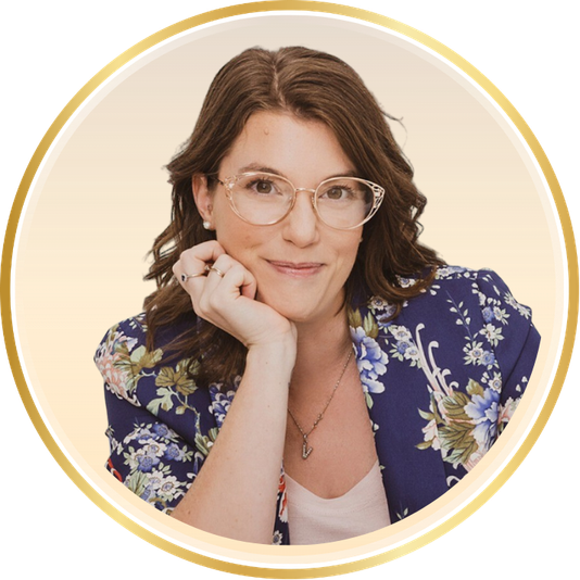 Portrait of a smiling woman with glasses in a floral blouse, resting her chin on her hand.