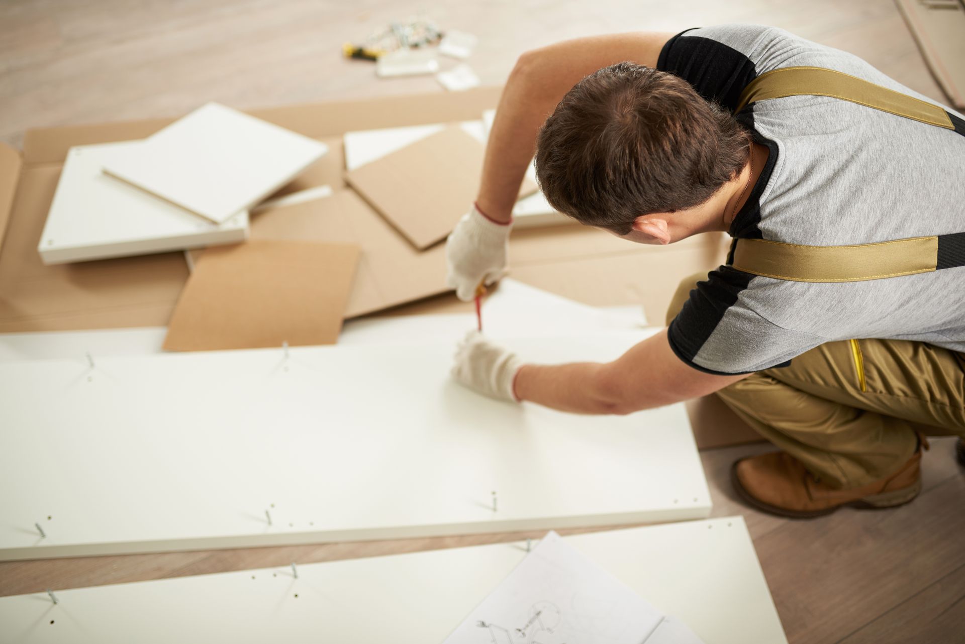 A man is kneeling on the floor working on a piece of wood.