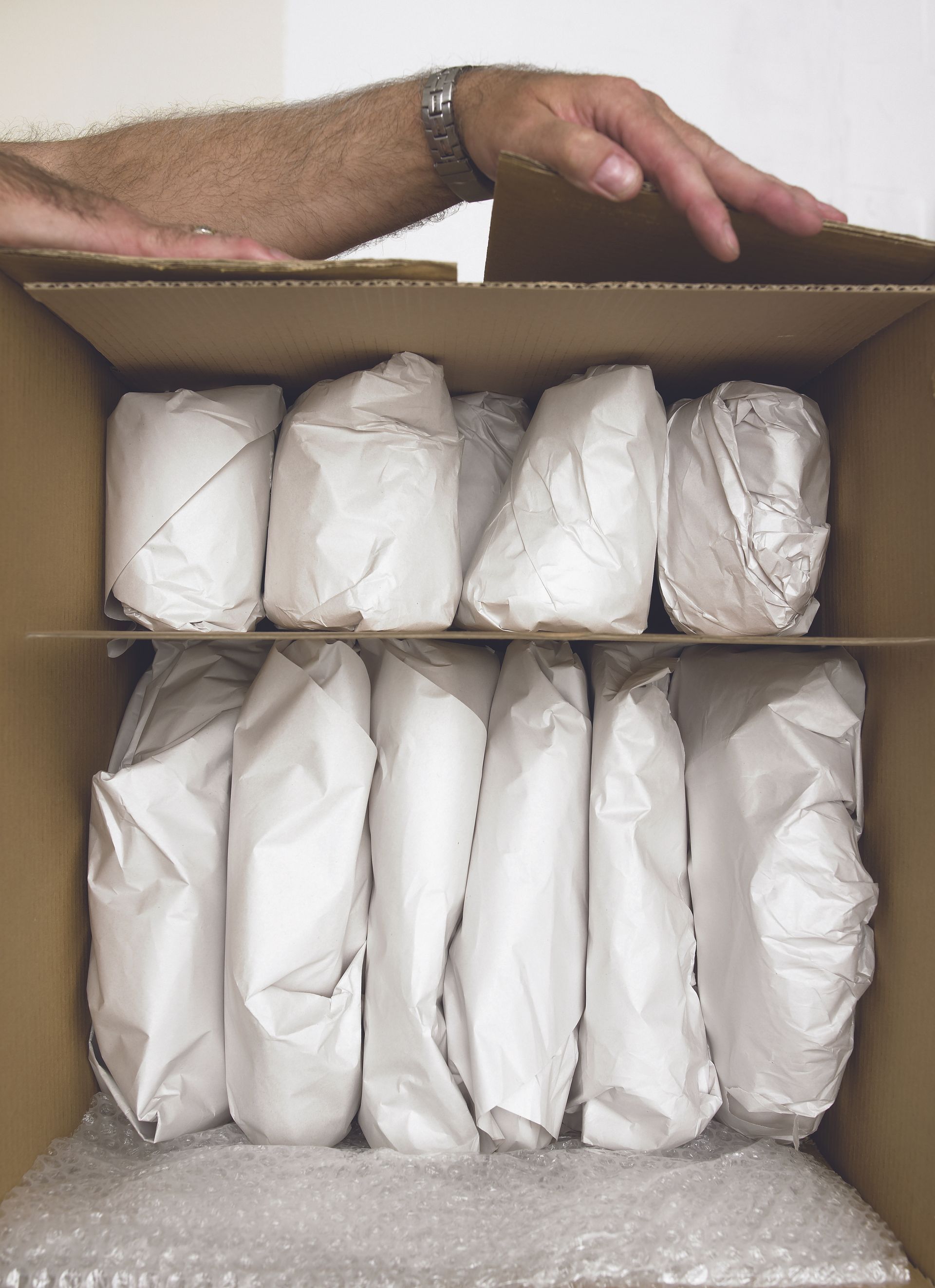 Boîte en carton remplie d'objets emballés, une main qui y plonge la main.