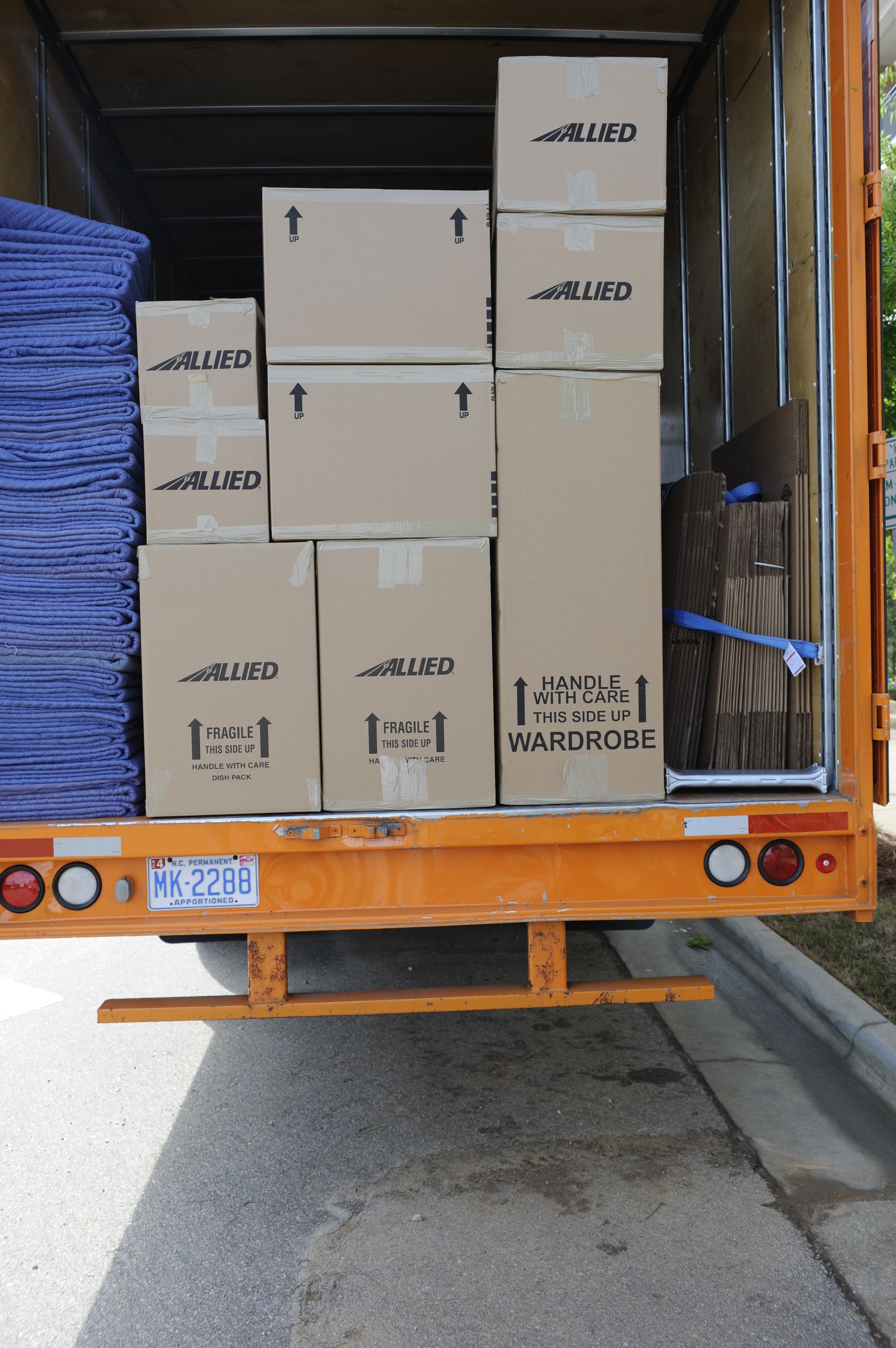 Camion de déménagement ouvert, rempli de cartons et d'objets pliés en bleu, sur le quai arrière.