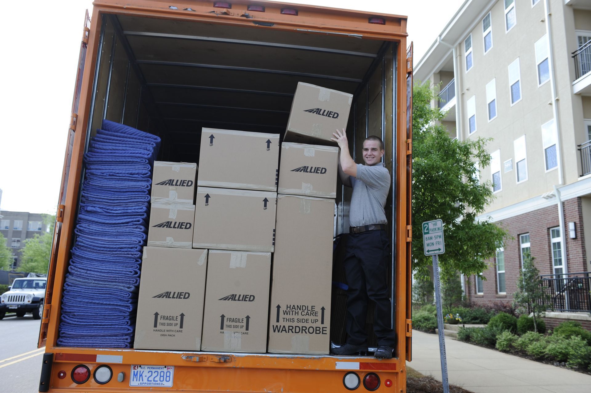 Un homme charge des cartons à l'arrière d'un camion de déménagement orange. Les cartons sont empilés ; environnement résidentiel.