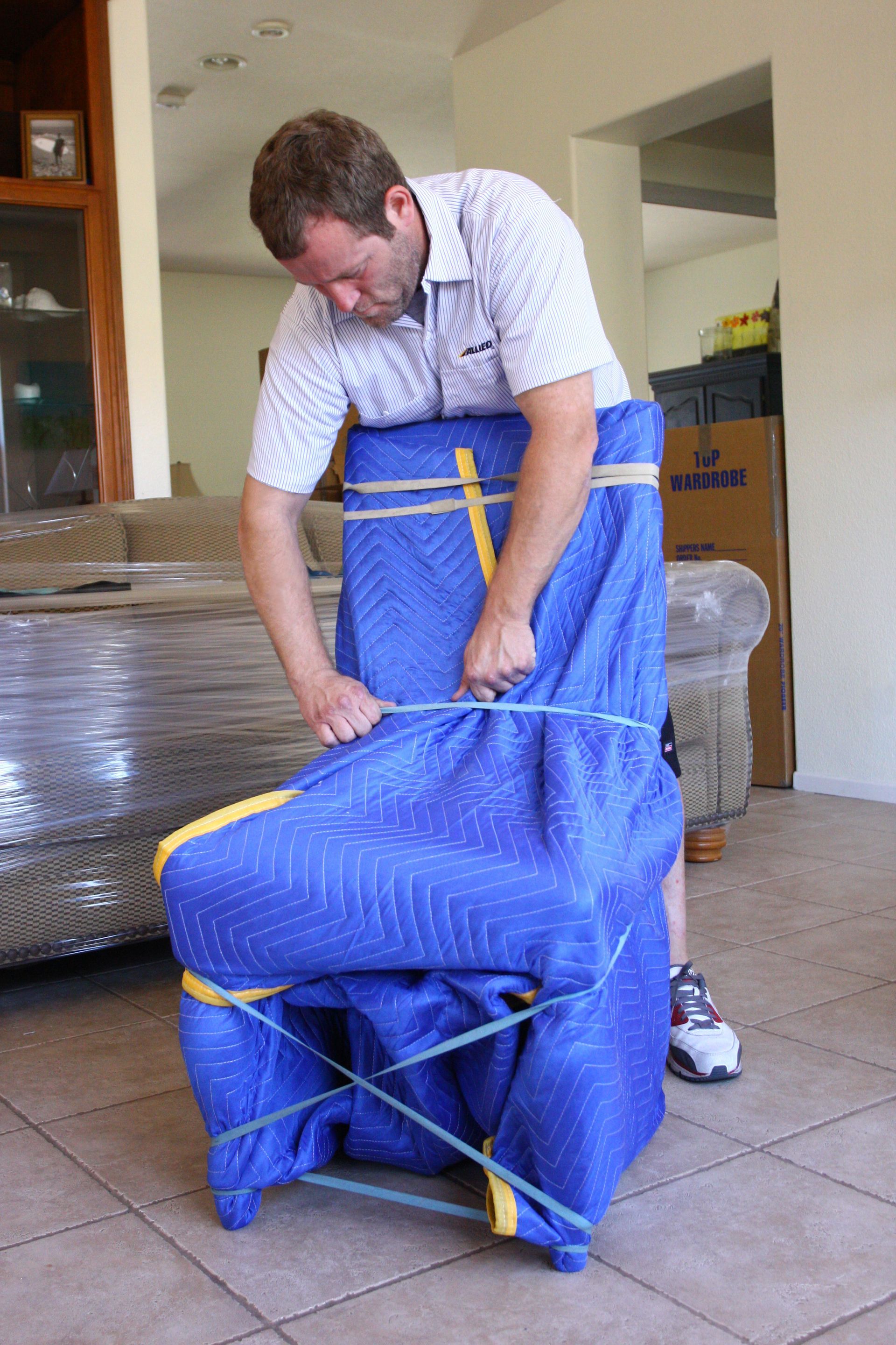 Un homme range une chaise emballée dans un film bleu à l'intérieur, en serrant des sangles jaunes autour.