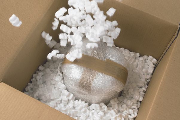 A cardboard box filled with packing peanuts and a piece of wood