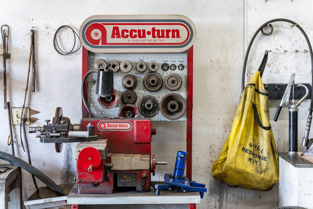 Accu-turn machine with tools hanging on a workshop wall and a yellow bag to the right