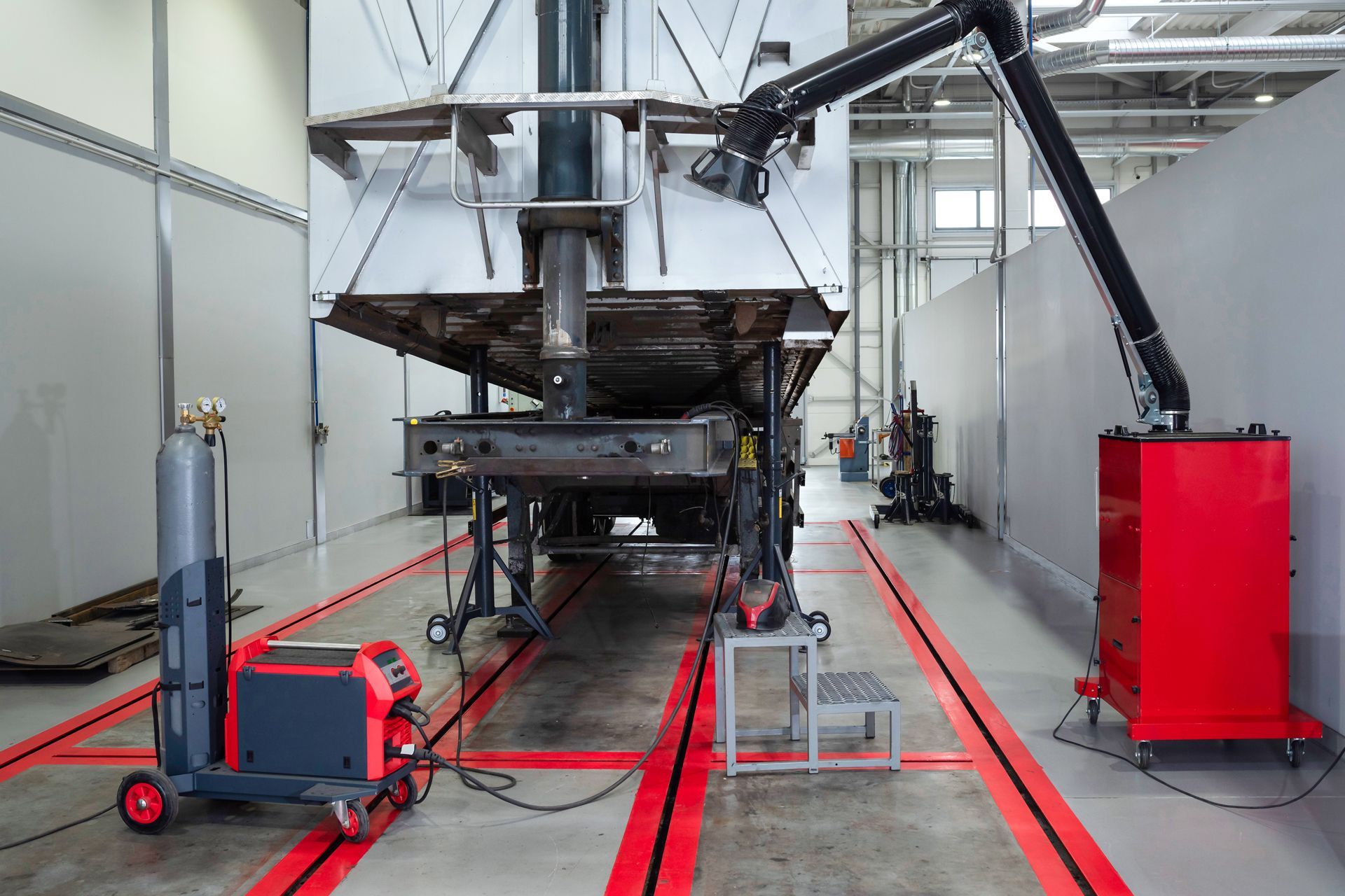 A large industrial workshop with welding equipment and a mobile fume extractor positioned near a suspended metal structure.