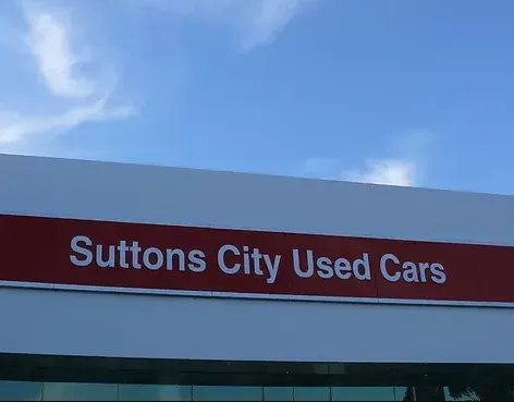 A red and white sign for suttons city used cars