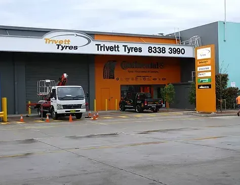 A truck is parked in front of a building that says trivett tyres