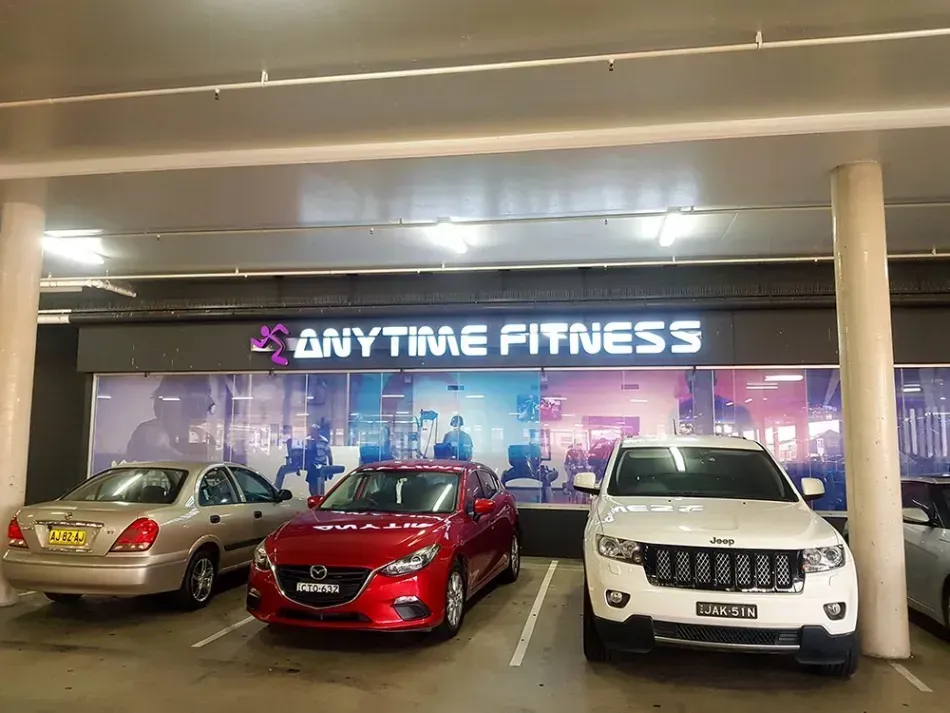 A row of cars are parked in front of an anytime fitness gym.