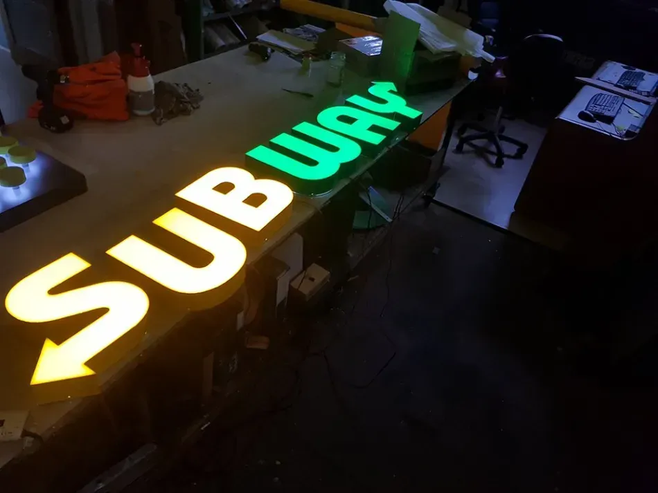 A subway sign is sitting on a table in a dark room.