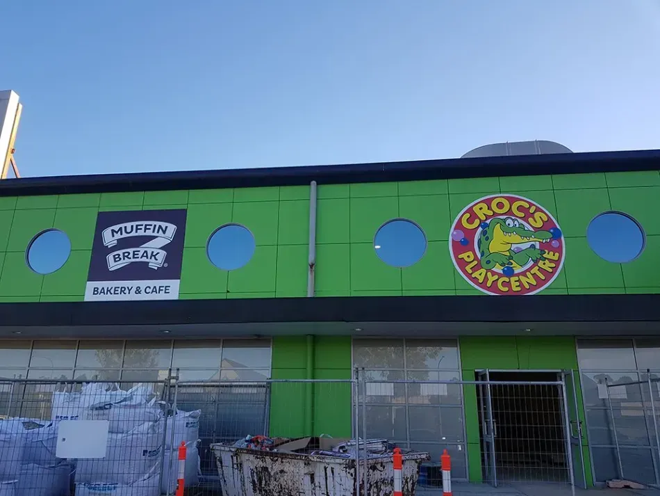 A green building with a sign on it that says crocs play centre.