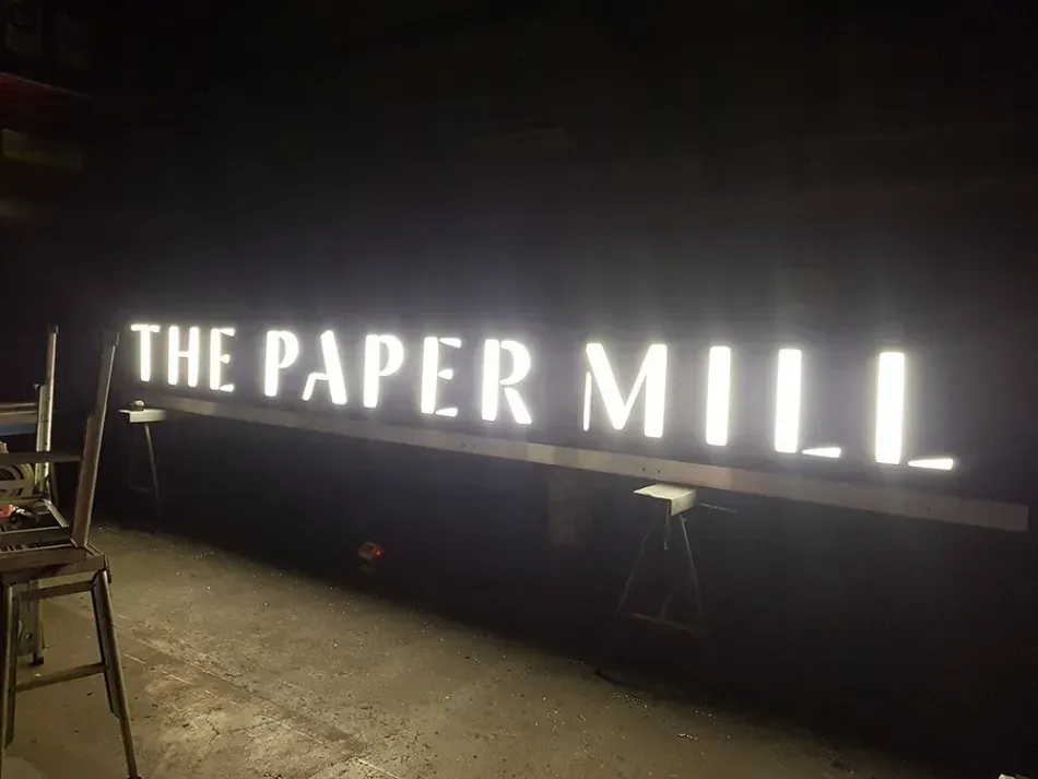 A large sign that says the paper mill is lit up in the dark.
