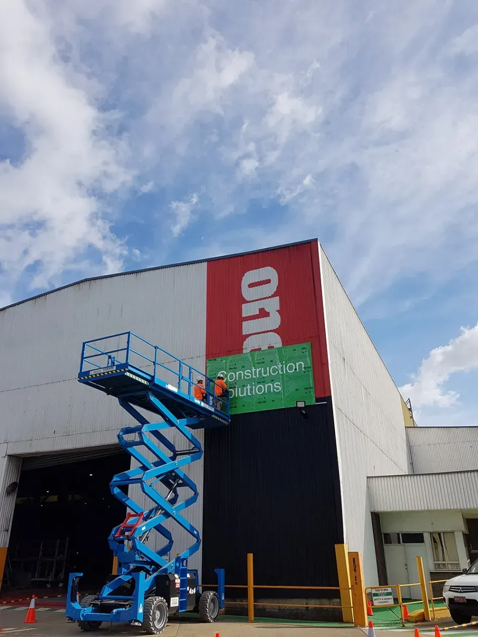 A man on a scissor lift is painting a sign on the side of a building.