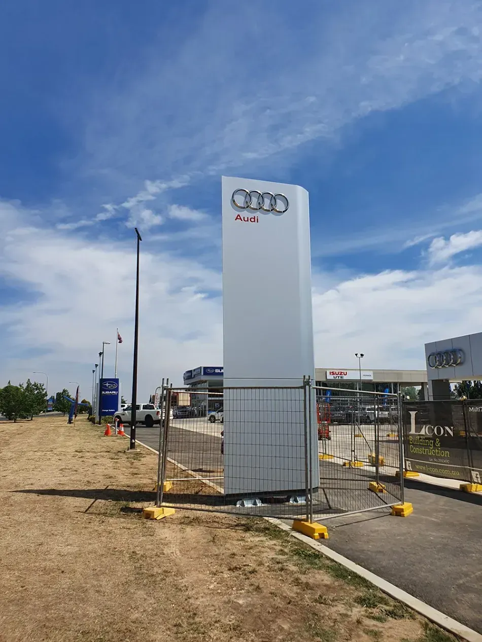 An audi sign is sitting in the middle of a dirt field.