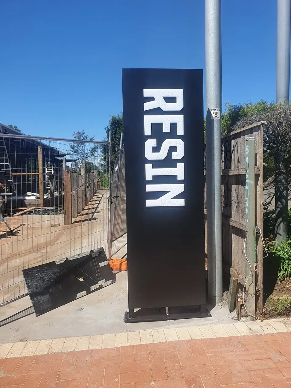 A large black sign with the word resin on it is sitting next to a pole.
