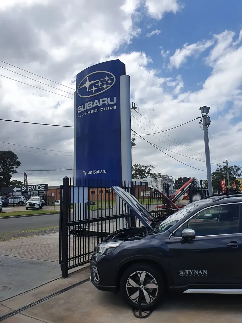 A subaru car with its hood open is parked in front of a subaru dealership.
