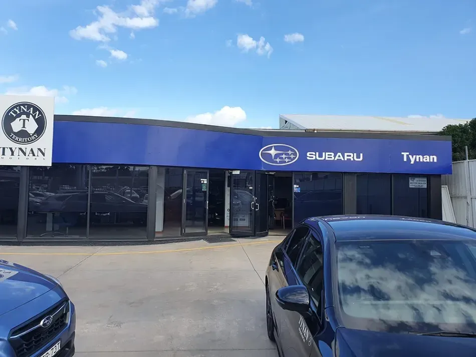 A blue subaru car is parked in front of a subaru dealership.