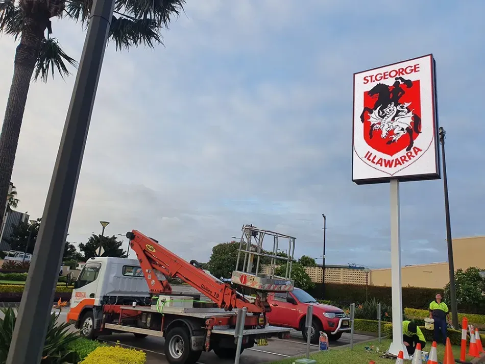 A truck with a crane attached to it is parked in front of a sign.