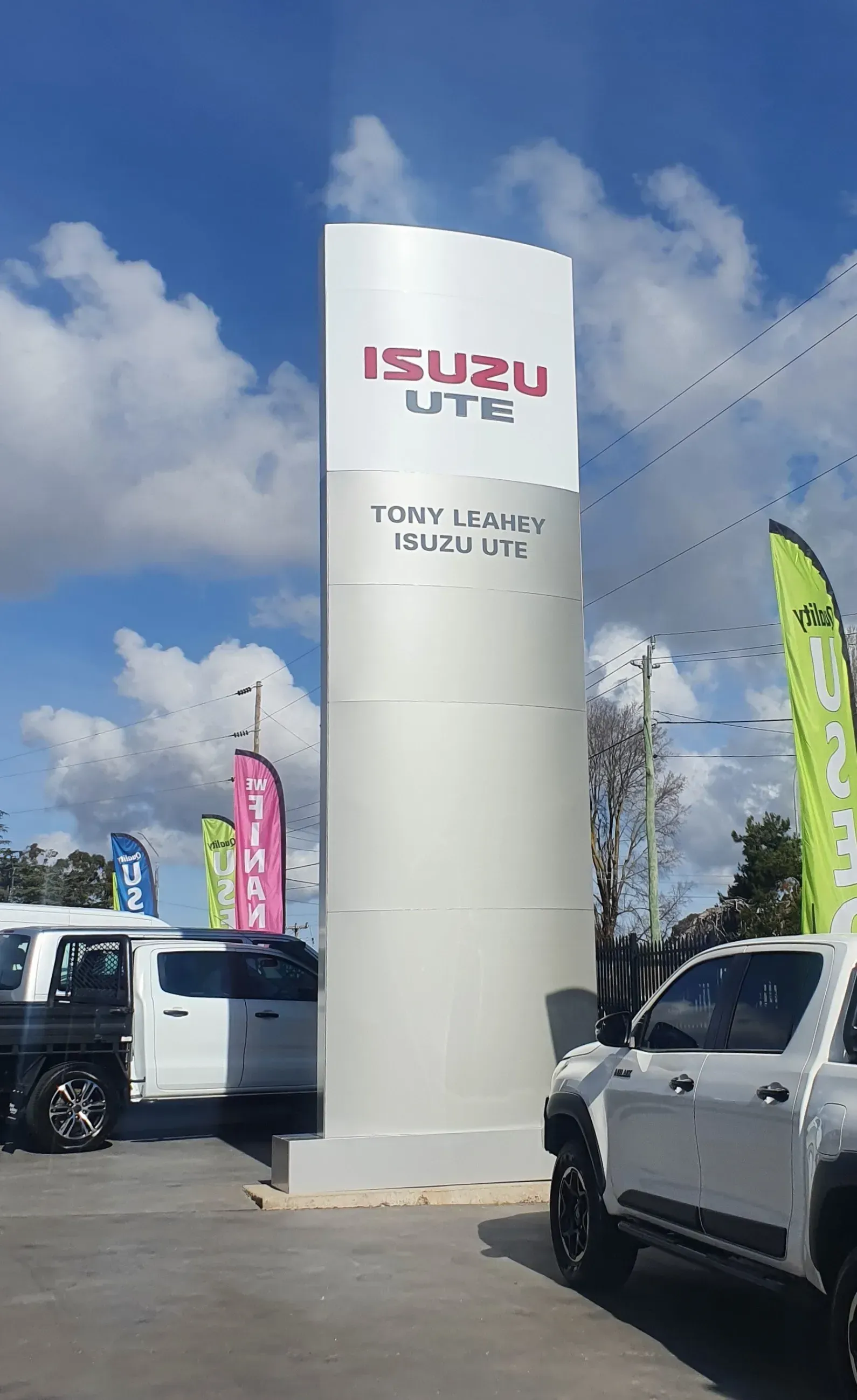 A white isuzu ute is parked in front of a car dealership.