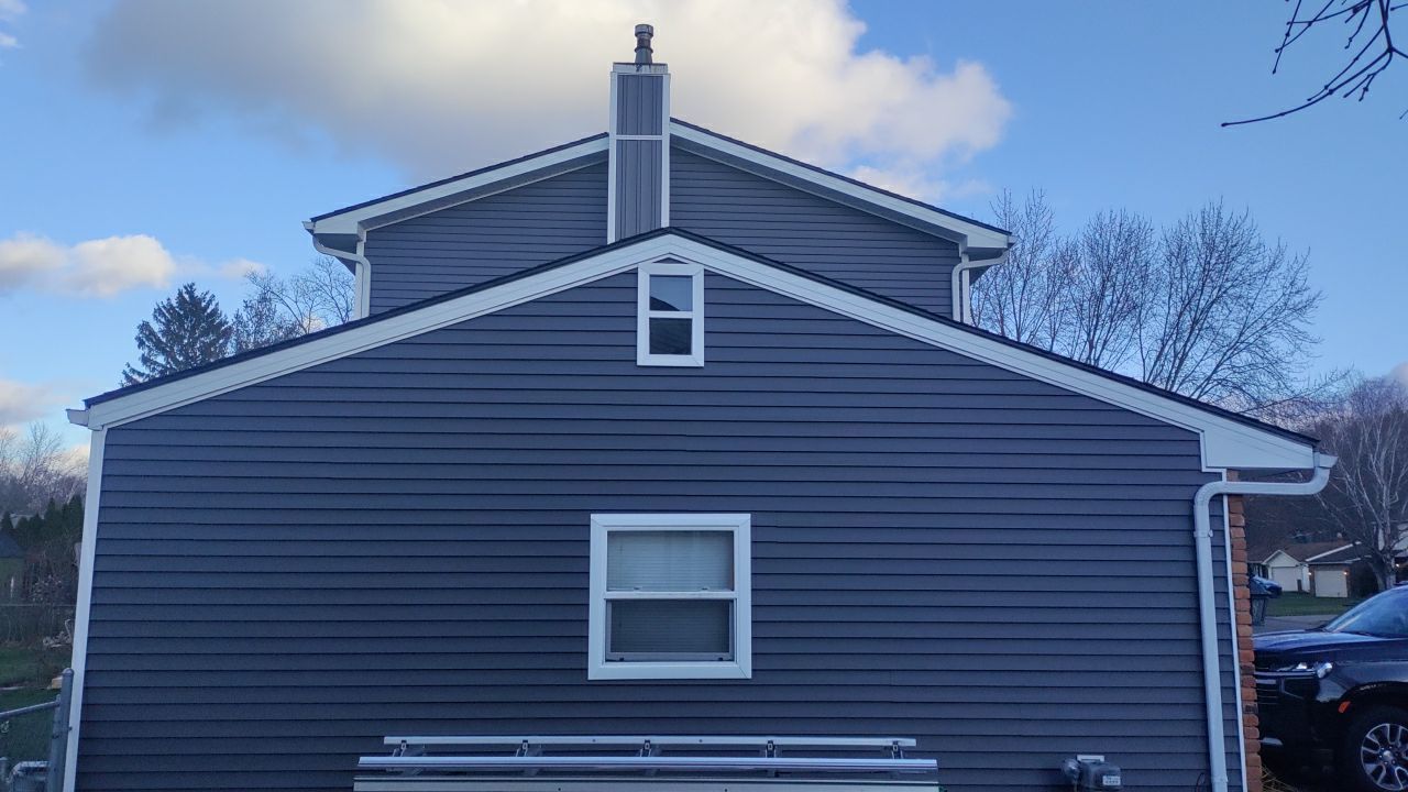 A gray house with a white trim and a chimney on the roof.